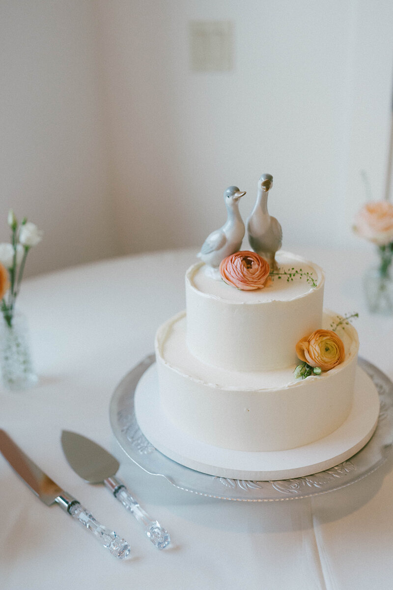 Photo of a wedding cake with flower details and cute goose toppers