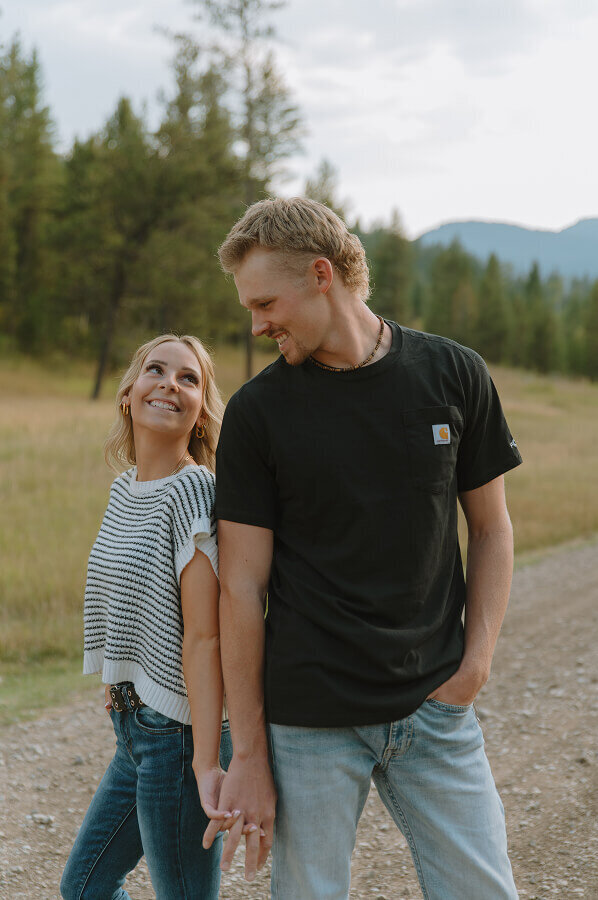 Couples photography in the mountains of eastern ID near Idaho Falls. Holding hands and standing back to back, a man and woman look into each others eyes and smile.