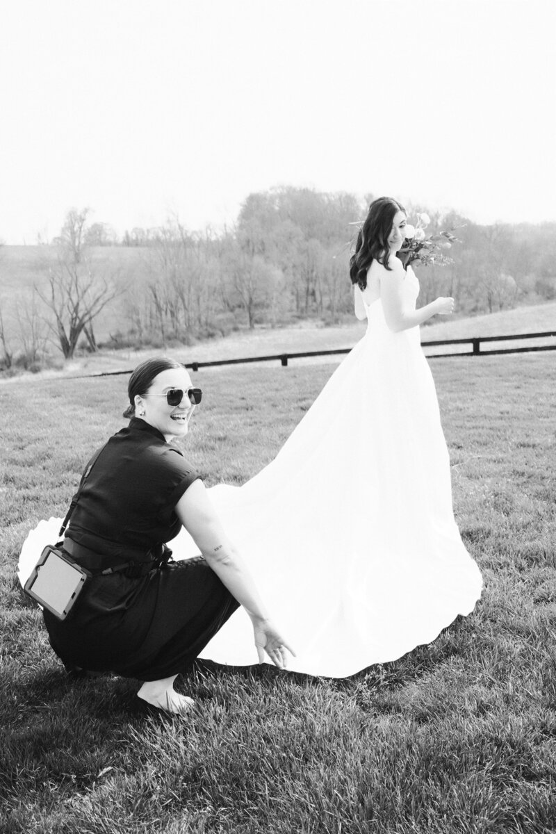 Wedding planner adjusts train on bride's dress on a farm in Tennessee