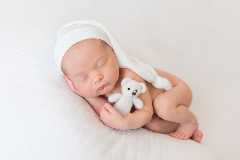 Newborn baby boy sleeping on his side with sleepy cap and teddy bear during studio newborn session.