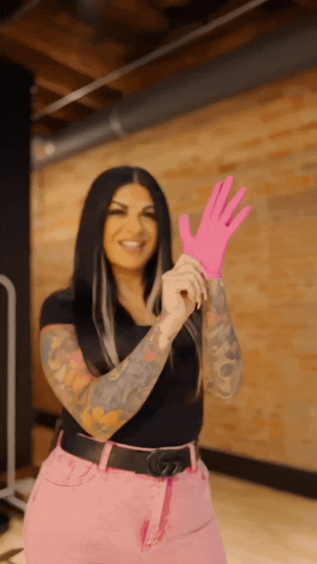 Santina wearing pink pants and a black shirt as she puts on pink hair dye gloves.