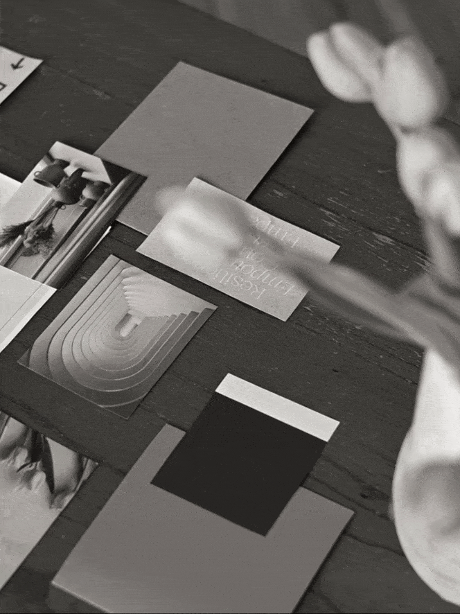 Design moodboard with various print materials in neutral tones, featuring abstract shapes, textures, and typefaces spread across a wooden surface.
