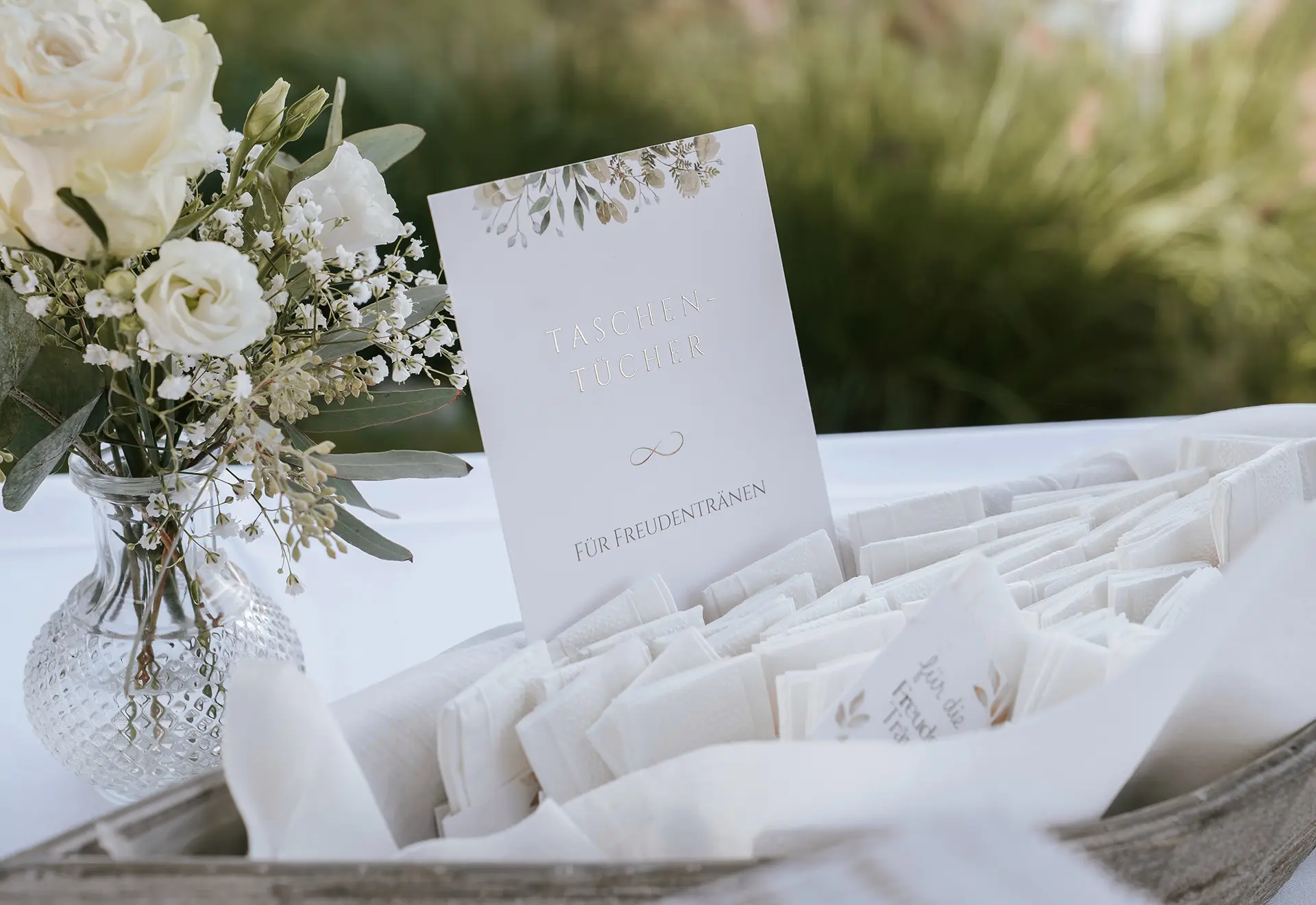Hochzeitsfotografie Schleswig Holstein – Detailaufnahme von Freudentränen-Taschentüchern und floraler Hochzeitsdeko im Strandrestaurant Marienbad.