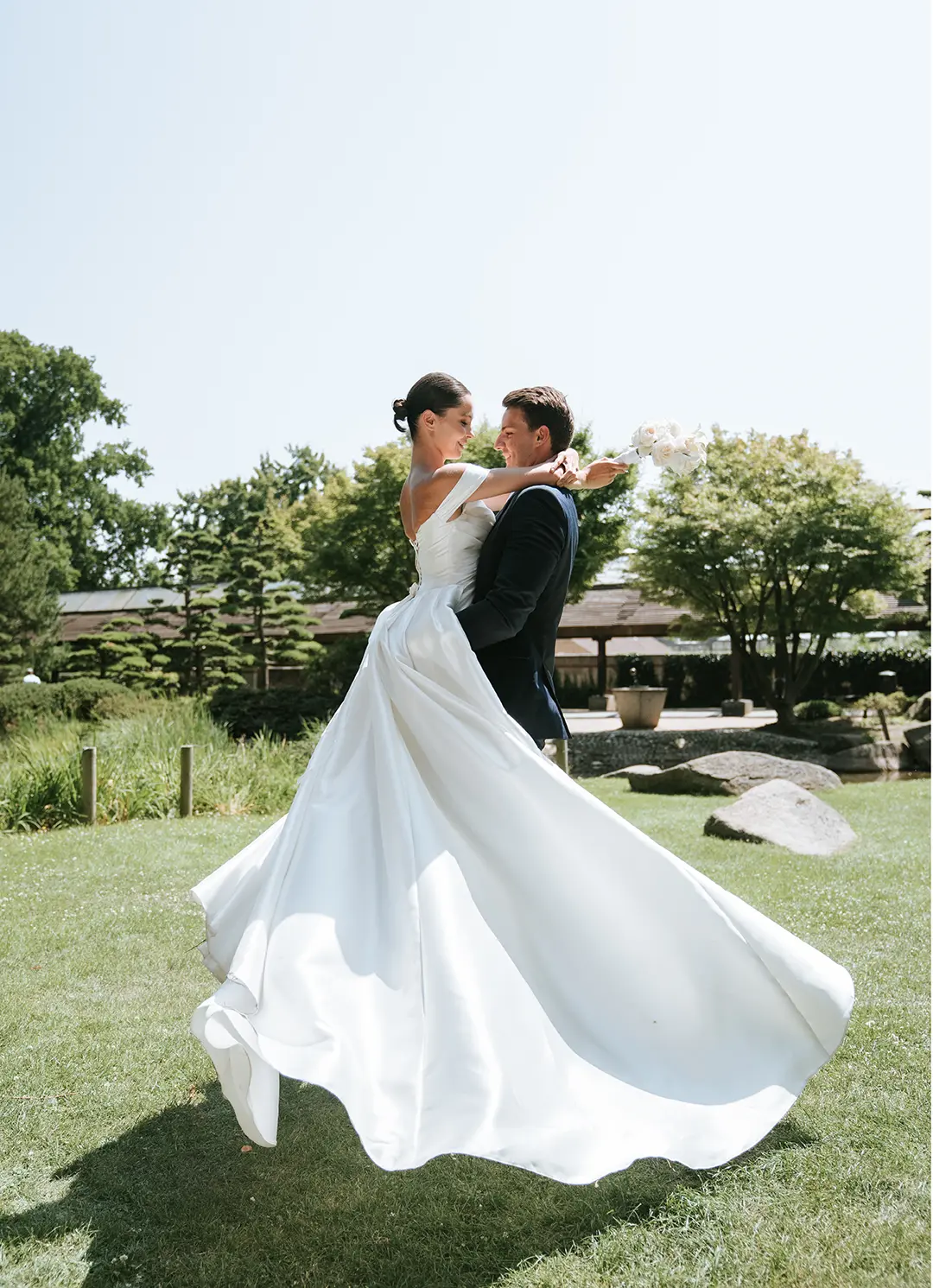 Der Bräutigam hebt die Braut, das weite Kleid schwingt groß über die Wiese, Bäume rahmen die Szene; natürliche hochzeitsfotografie und reportagefotografie hochzeit