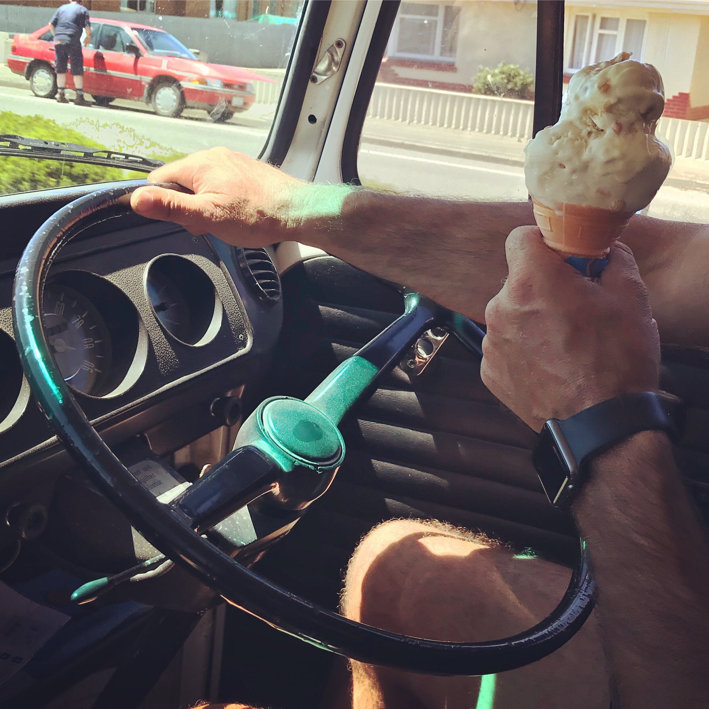 Man holding a hokey pokey ice cream cone while driving a teal VW Kombi van on a sunny Southland day.