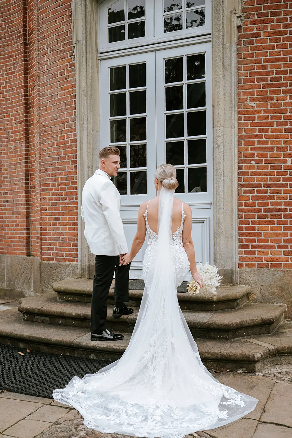 Braut und Bräutigam gehen Hand in Hand Stufen eines Backsteingebäudes hinauf; hochzeitsfotograf für schloss-hochzeit erstellt klassische hochzeitsfotos und exklusive Brautpaarportraits Hamburg