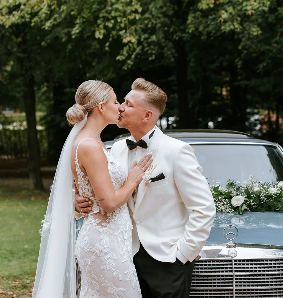 Brautpaar küsst sich vor geschmücktem Oldtimer im Park; exklusive Brautpaarportraits Hamburg treffen auf hochzeitsfotografie mit stil und klassische hochzeitsfotos