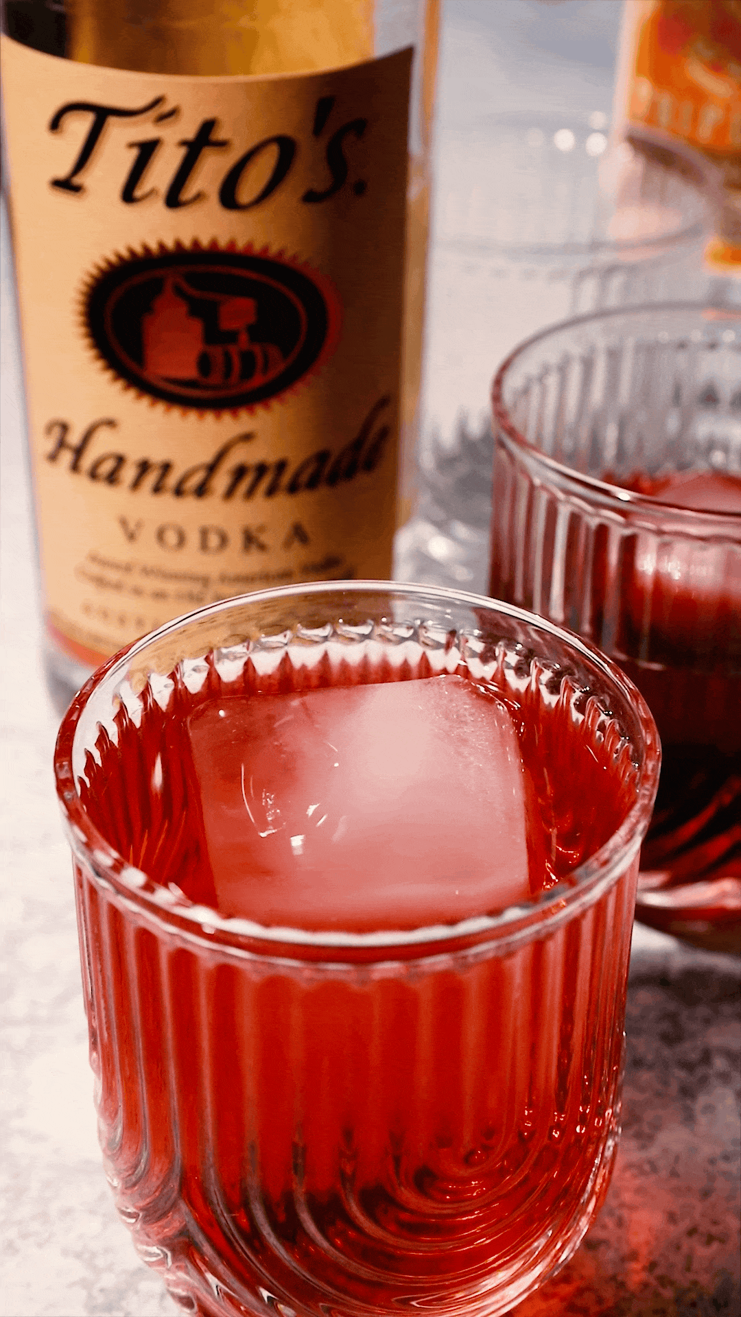 A close-up of a vibrant red cocktail served in a ribbed glass, with a bottle of Tito’s Handmade Vodka in the background. Captured by Austin-based photographer Mica McCook, this image highlights the rich color and texture of the drink, showcasing Mica’s attention to detail in food and beverage photography.