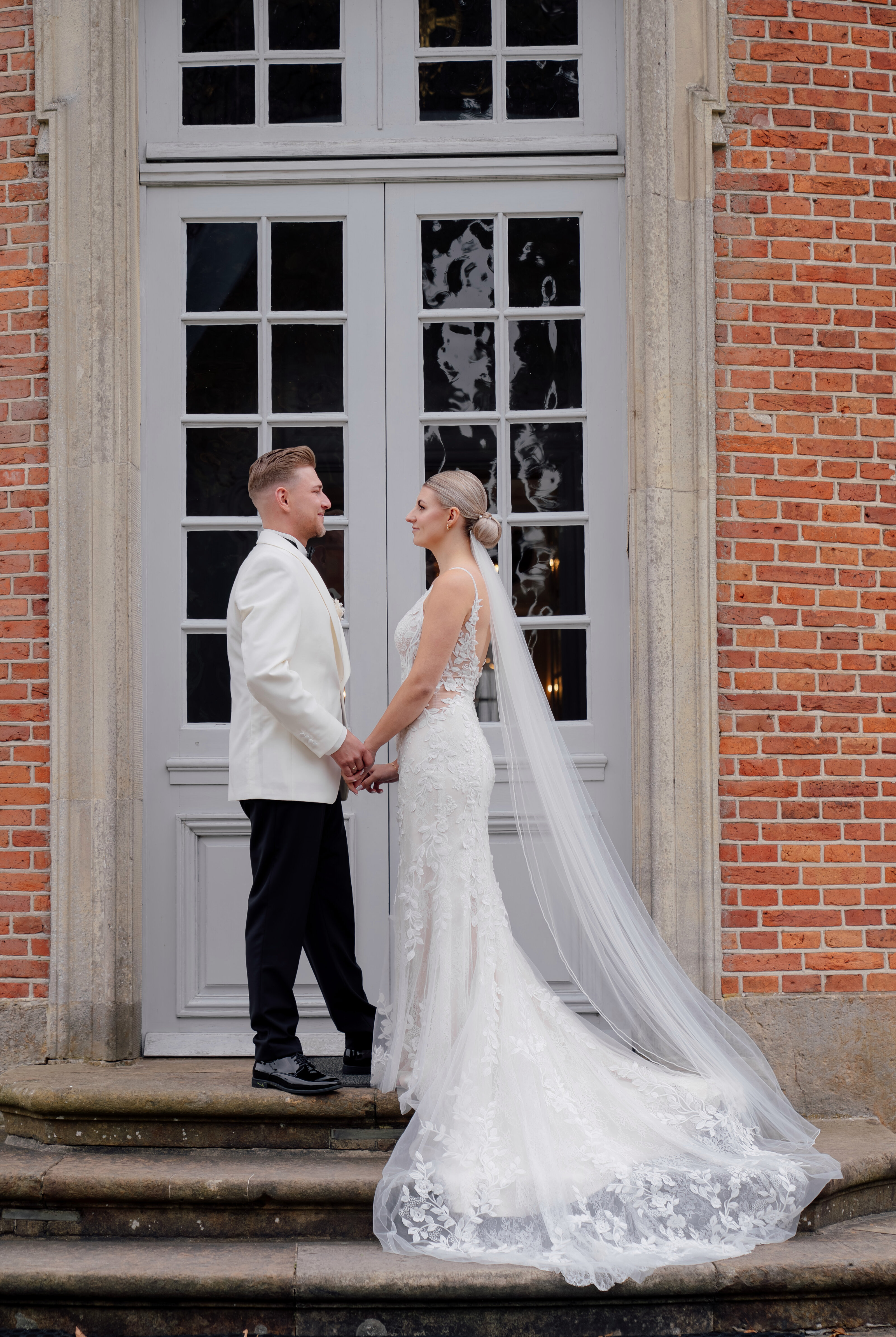 Der Bräutigam hält die Braut liebevoll im Arm, Holzstreben und Grün schaffen einen intimen Rahmen. Hochzeitsfotografie mit Stil und reportagefotografie hochzeit harmonisch vereint