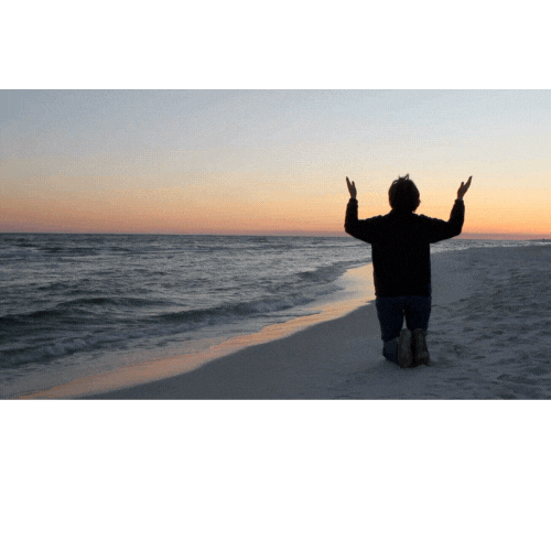 woman praying on a beach at sunset