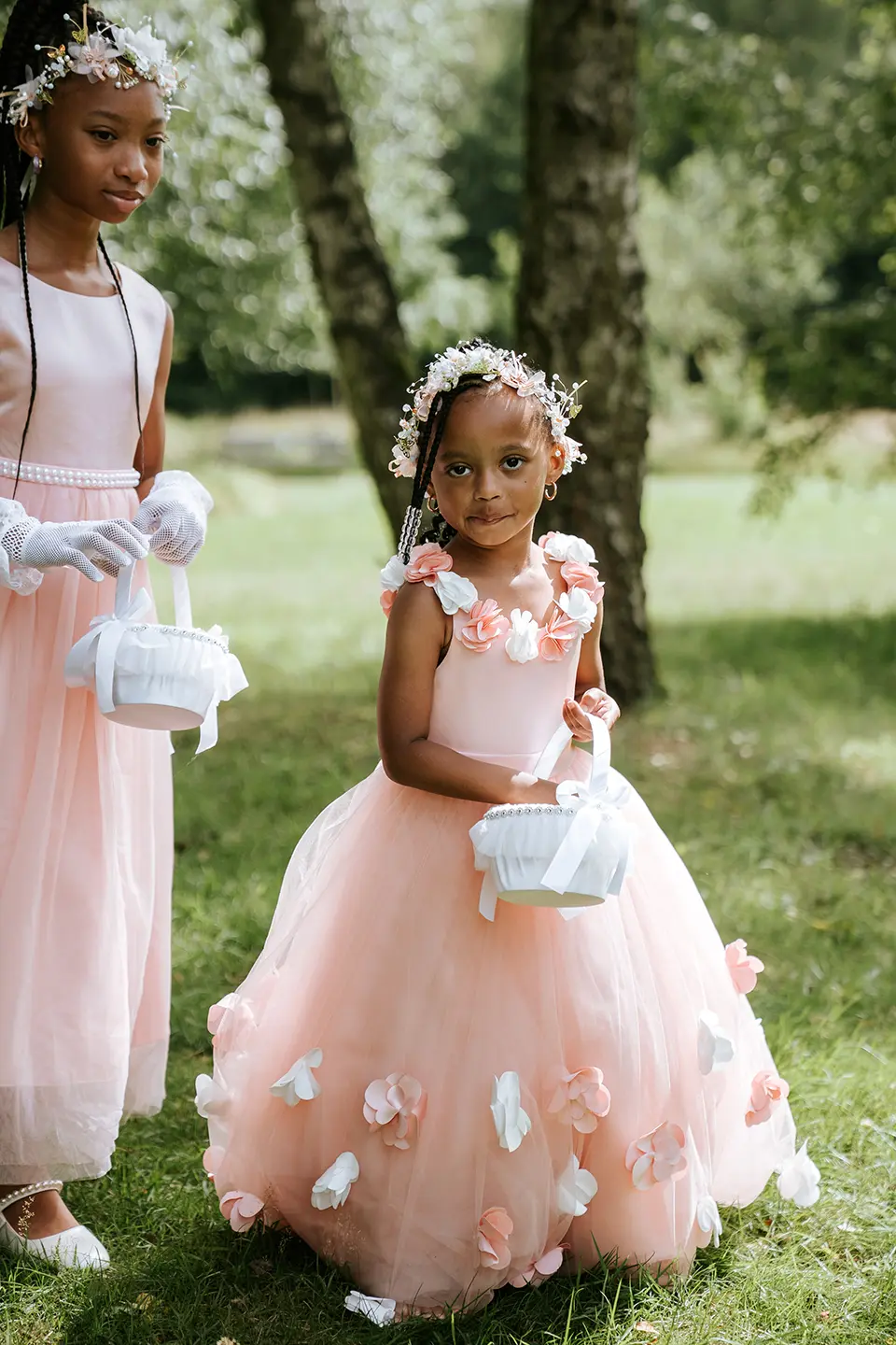 Zwei Mädchen mit Blütenkränzen tragen weiße Körbchen und Tüllkleider in Rosé. Emotionale Hochzeitsbilder und reportagefotografie hochzeit mit liebevollen Details im Freien