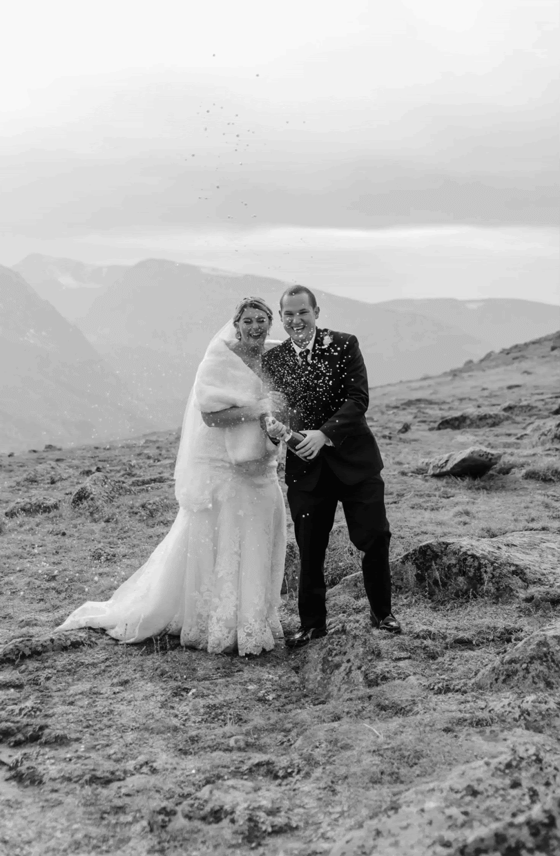 groom sprays champagne on top of a mountain while bride laughs