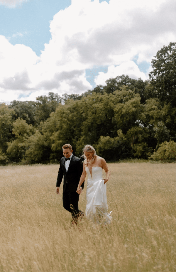 a bride and groom walking in a field