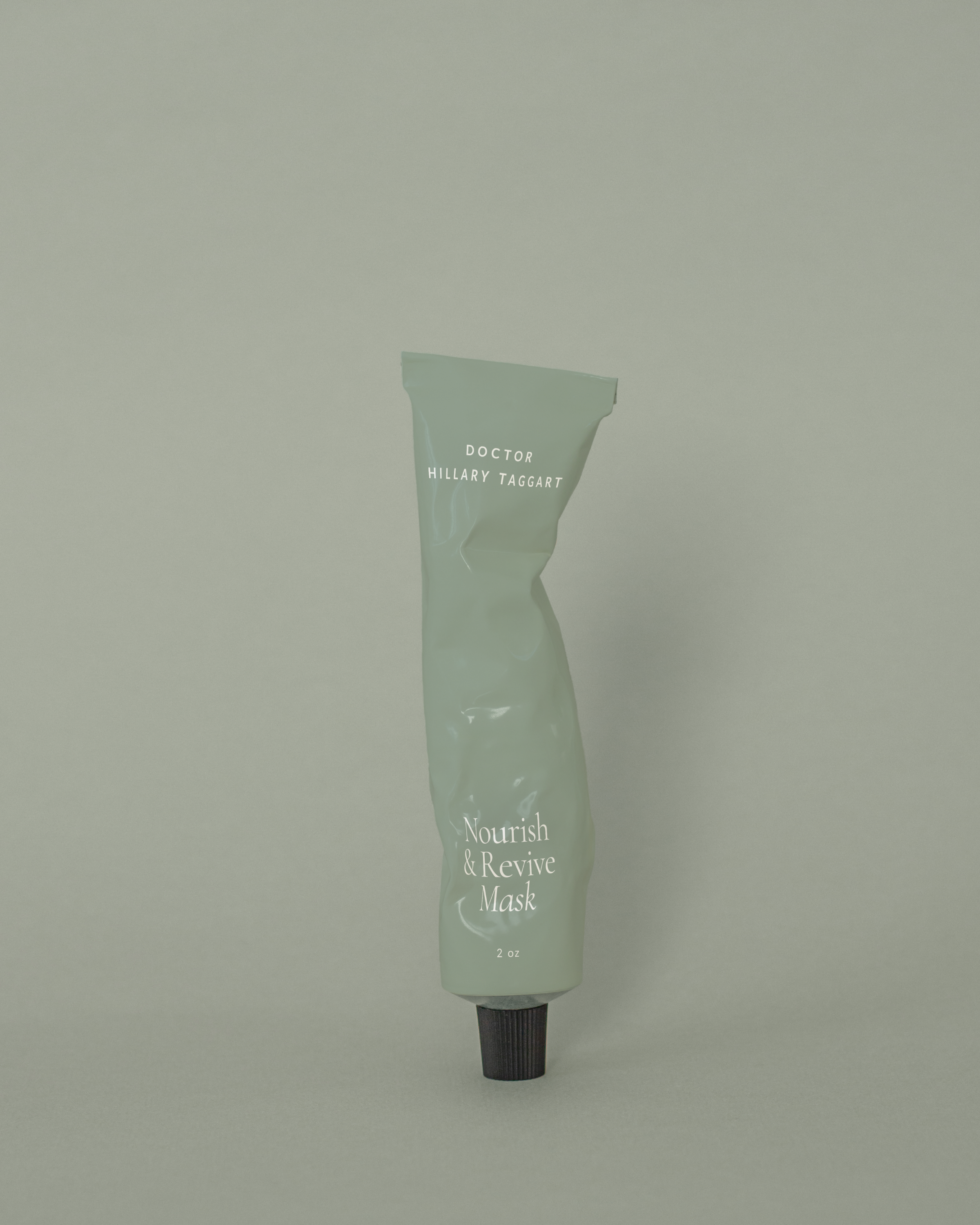 Single sage-green tube labeled ‘Nourish & Revive Mask’ set on a matching background, an example of cohesive beauty brand identity in skincare packaging.