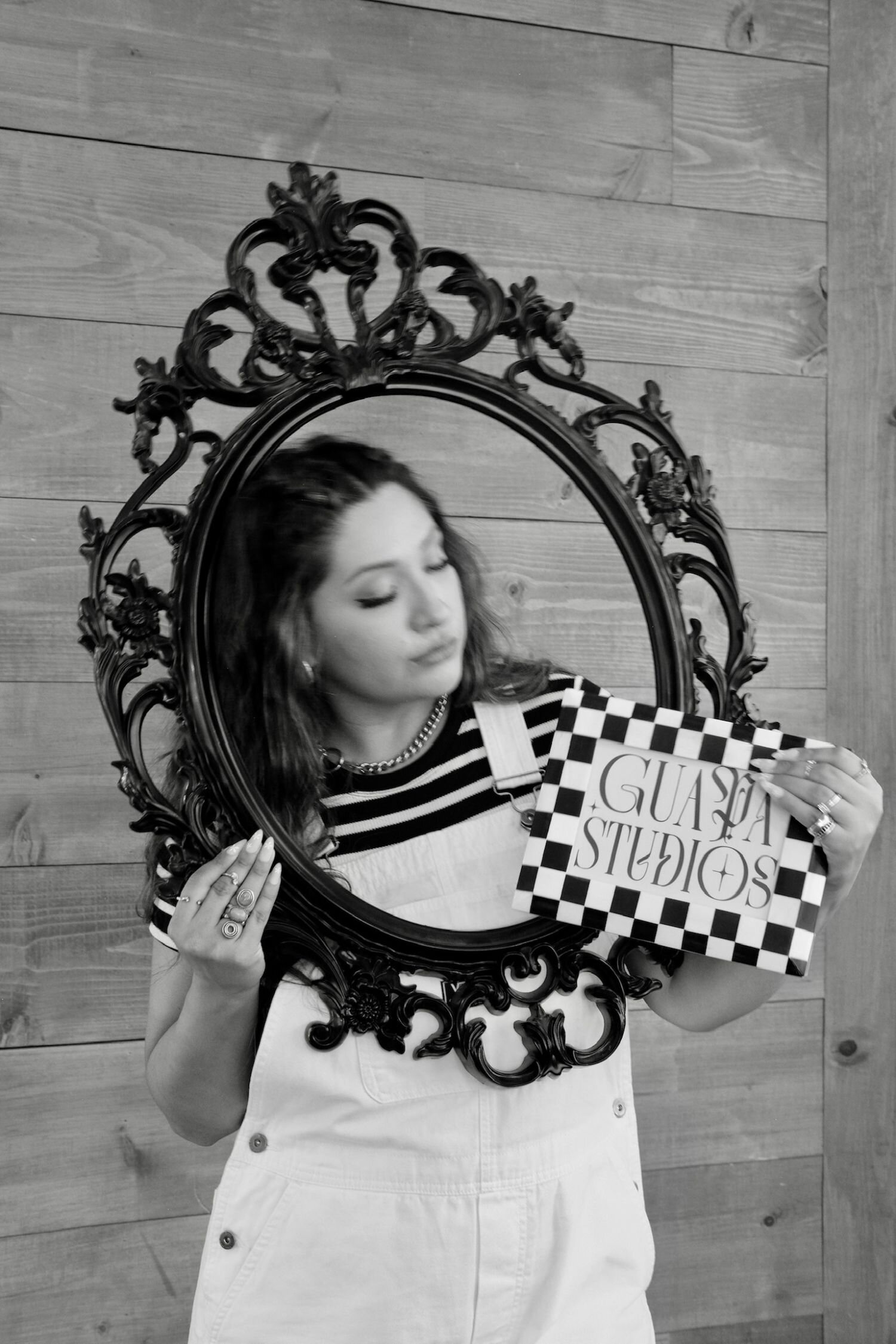 black and white pic of latina web designer, joyce holding black frame and guapa studios logo next to her