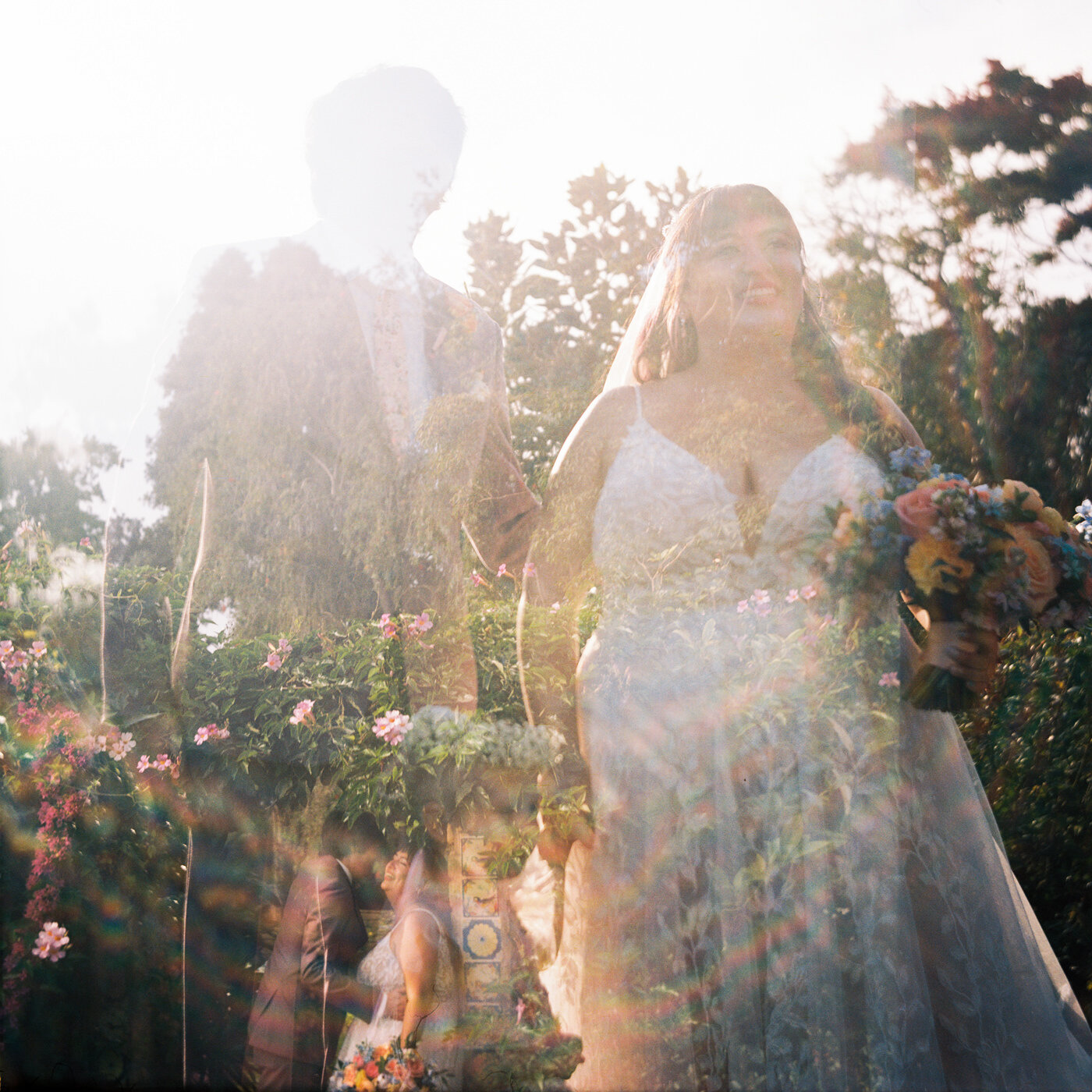 an artistic double exposure on film where the top layer shows a bride and groom looking off camera and smiling, and the bottom layer shows a natural landscape, and a smaller version of the bride and groom embracing and laughing with a sun-flared rainbow circling the image
