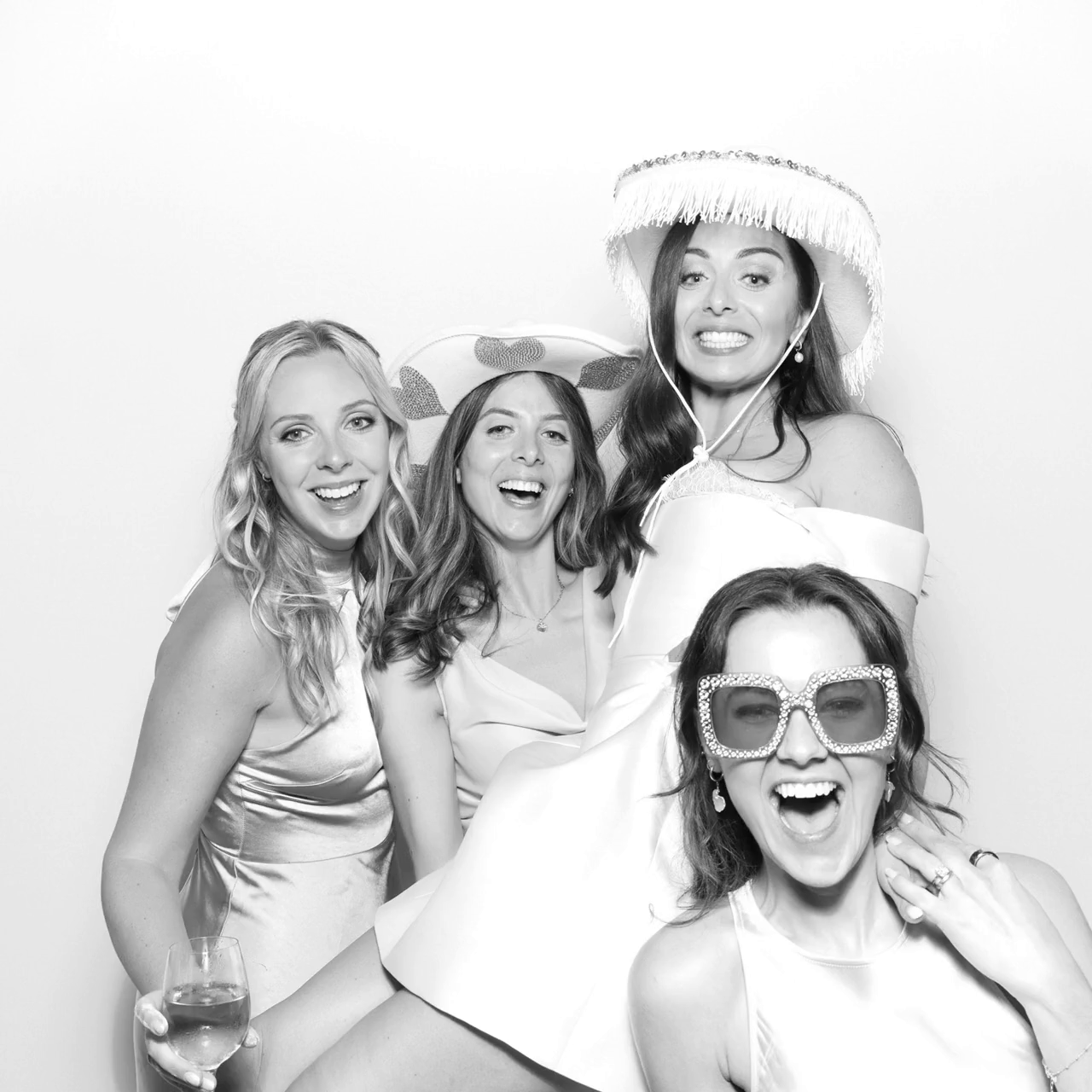 Black and white filter for a print with a group of guests and the bride, posing against a white backdrop, during a wedding party entertainment, for Mad Hat Photo Booth Farleigh House