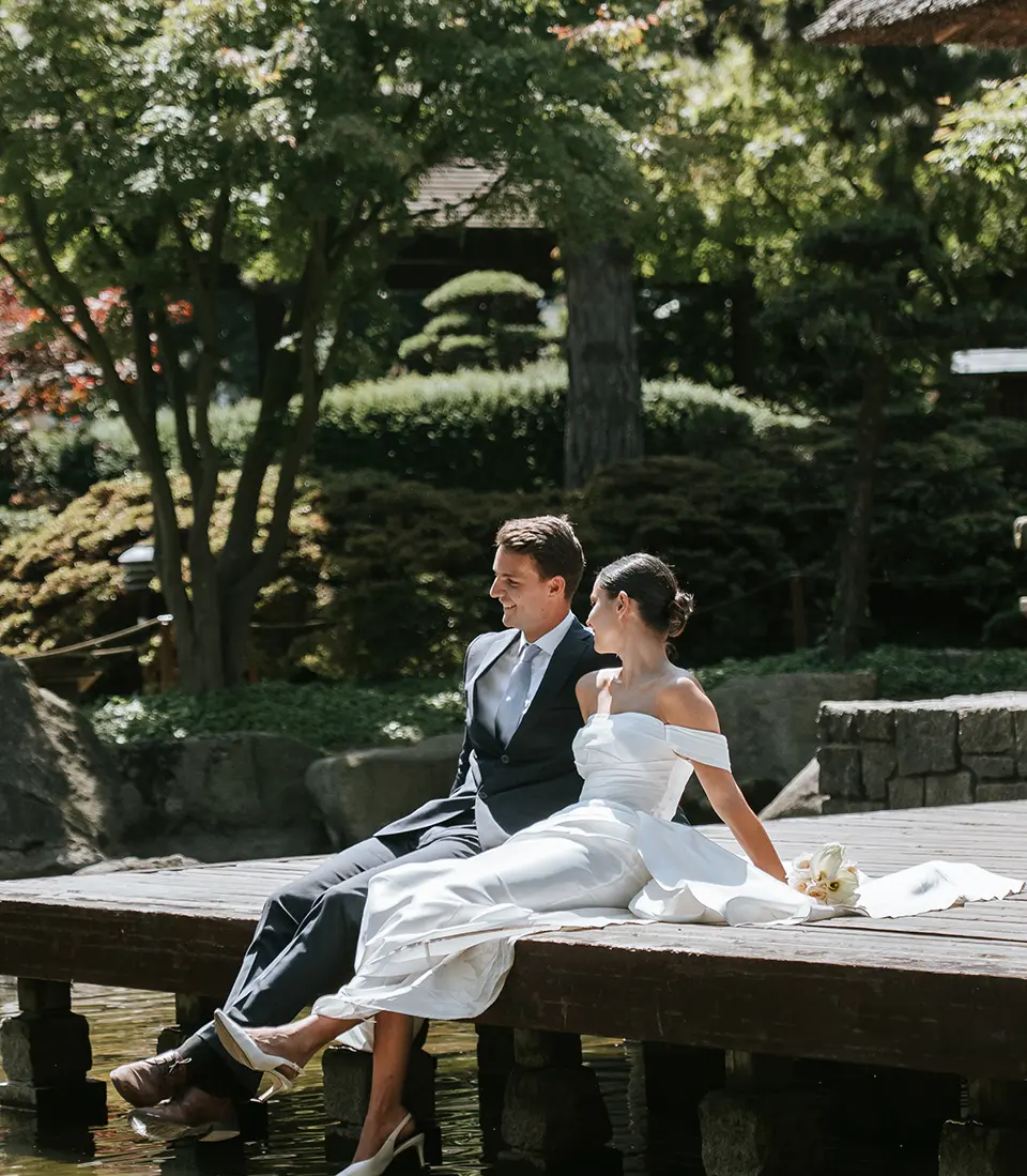 Braut und Bräutigam sitzen entspannt am Holzsteg über dem Teich, umgeben vom japanischen Garten in Planten un Blomen; natürliche hochzeitsfotografie und hochzeitsbilder draußen