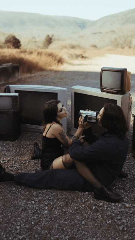 couple sitting on the ground surrounded by old tvs
