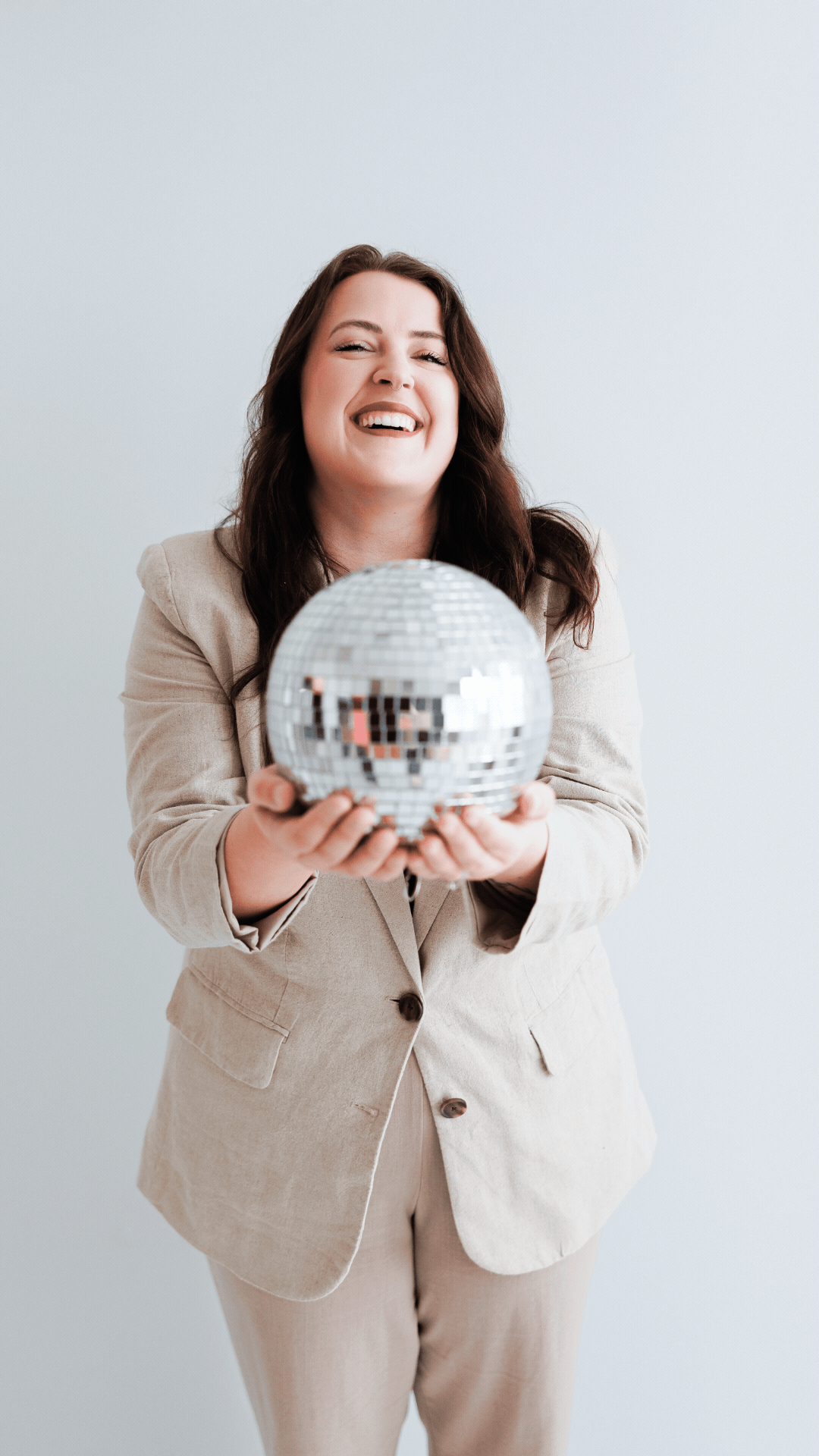This is a gif of Mariah of Moonlight Brand Design holding a disco ball and laughing. She is wearing a tan suit. 