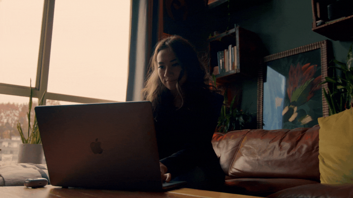 young woman sits on a couch while working on her laptop