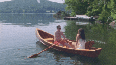 Super 8 film still of a couple eloping in Connecticut, rowing across a peaceful lake in a wooden canoe on a warm summer day — captured by a vintage wedding videographer.