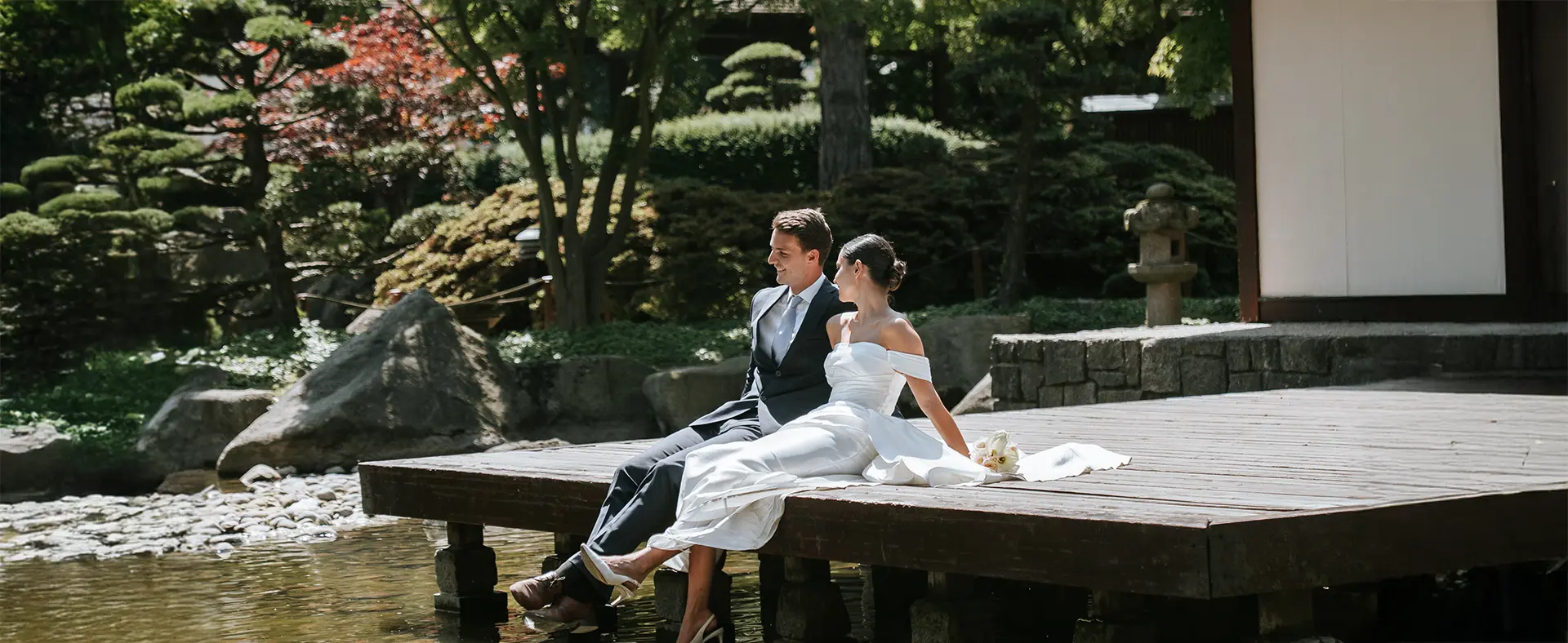 Braut und Bräutigam sitzen entspannt am Holzsteg über dem Teich, umgeben vom japanischen Garten in Planten un Blomen; natürliche hochzeitsfotografie und hochzeitsbilder draußen
