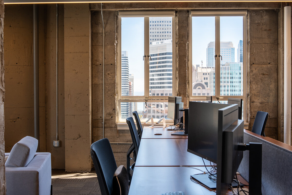 Industrial workspace with exposed concrete walls, wood desks, and large windows overlooking the city.