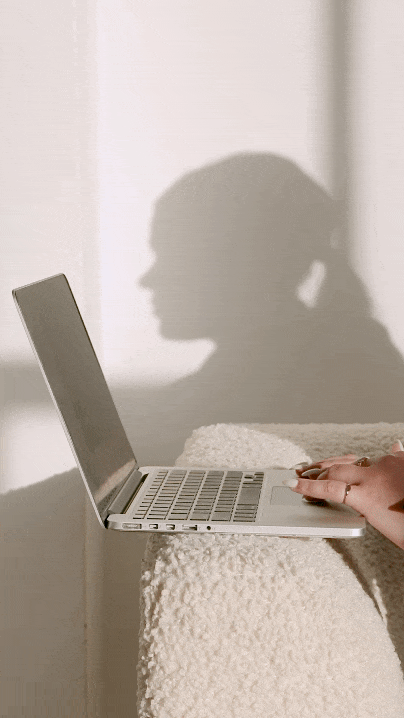 Hands typing on a laptop with a soft shadow silhouette of a person against a light wall.