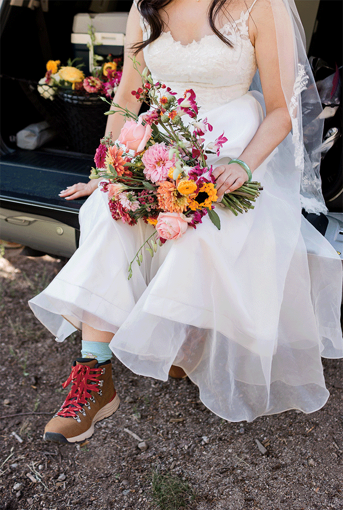 A bride sits on the tailgate of their Toyota, while swinging her feet playfully while on her mountain wedding. 
