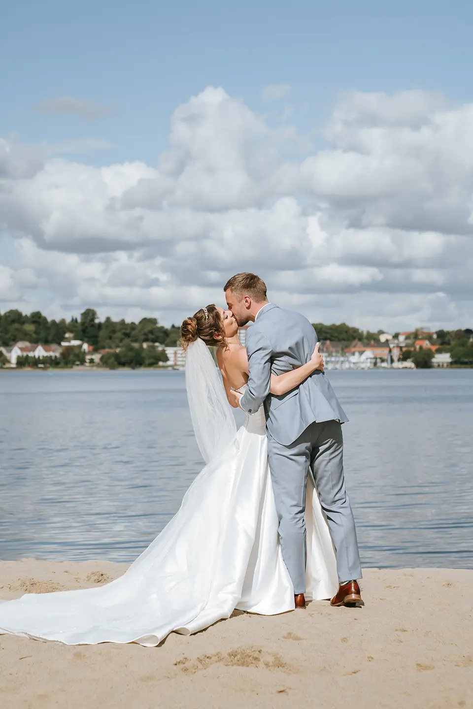 Braut und Bräutigam küssen sich am Strand vor ruhiger See; fotograf für hochzeit am strand liefert hochzeitsbilder draußen und kreative Hochzeitsfotografie Hamburg