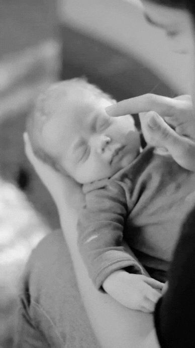 Black-and-white photo of a newborn sleeping peacefully while a finger gently touches their nose