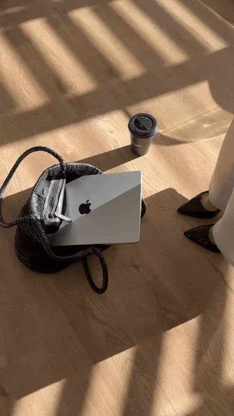 Branding expert and creative director placing a laptop into a woven black tote with coffee in hand—capturing the aesthetic and daily rhythm of a brand strategist and designer behind the scenes.