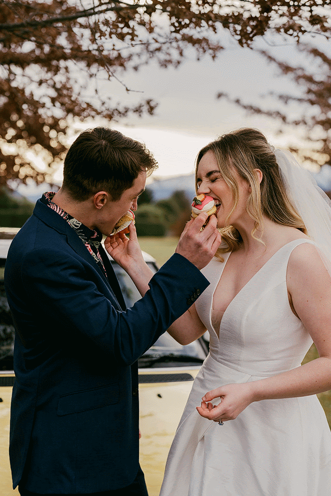 Bride and groom in animation feeding each other cupcakes and laughing with joy