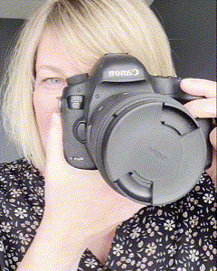 Blonde light skinned woman close up with her camera as a GIF. She holds up camera, takes it down and smiles.