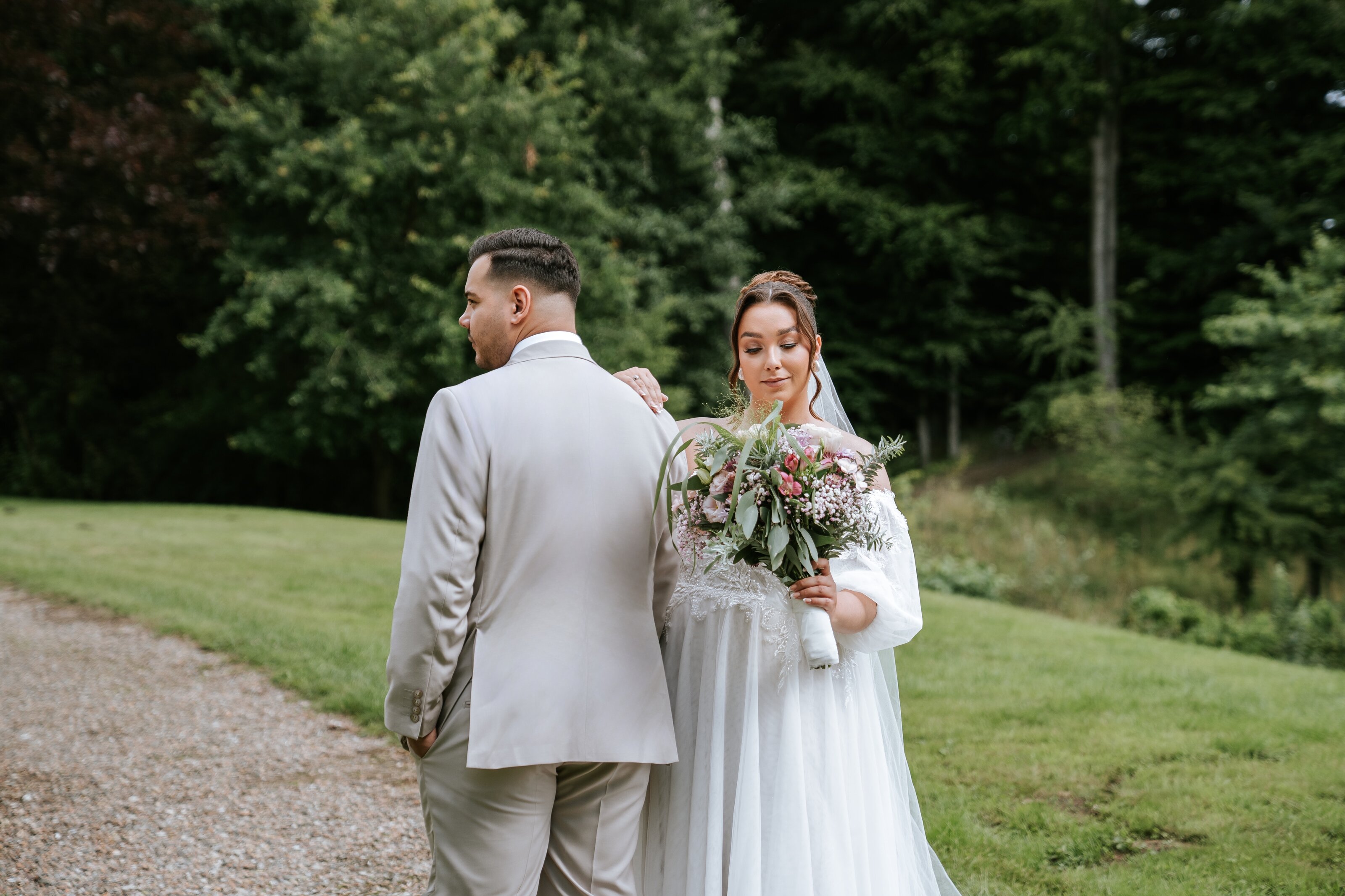 Braut im Profil mit langem Schleier, den weißen Rosenstrauß sanft am Gesicht; natürliche hochzeitsfotografie und fine art hochzeitsfotografie im blühenden Garten
