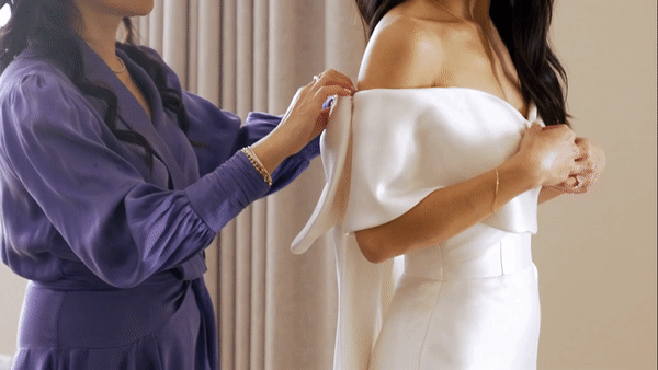 Mother of the bride helps her daughter put on wedding gown