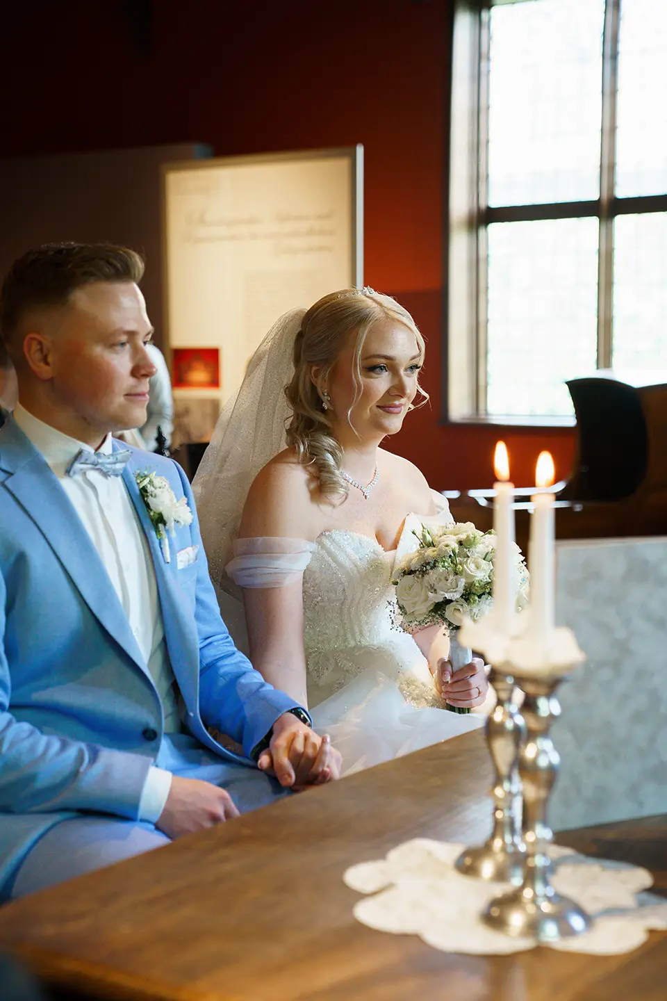Hochzeitsbilder Standesamt – Braut und Bräutigam sitzen während der standesamtlichen Trauung bei Kerzenschein.