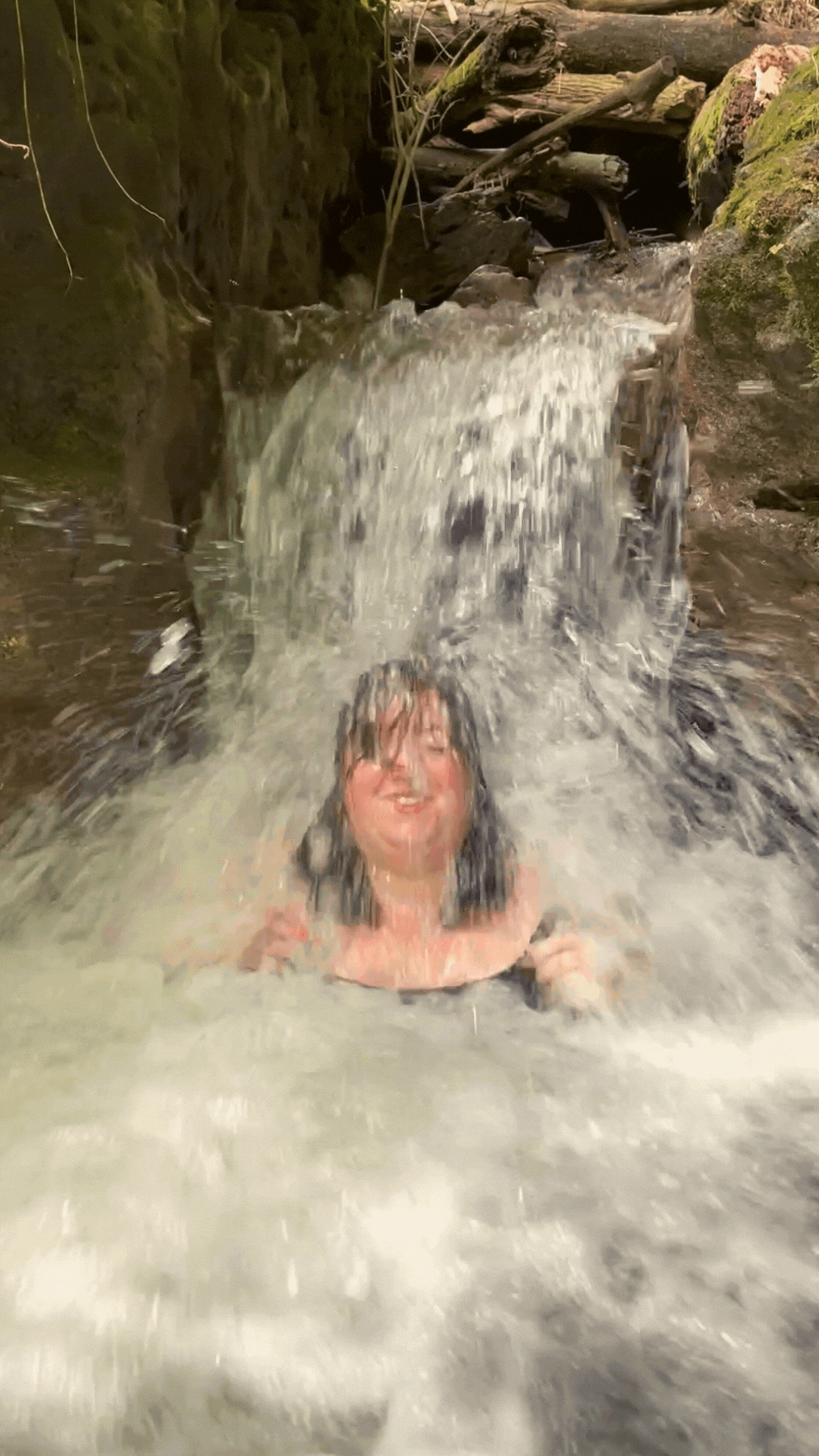Website designer for videographer comes out from under a waterfall laughing and smiling as she pushes water out of her face | Verbena Collective
