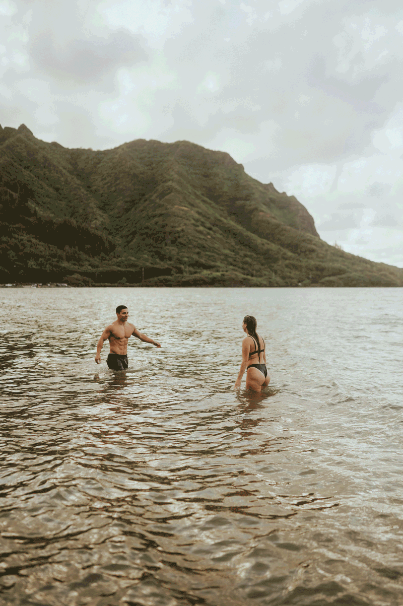 Husband and Wife walk towards each other in the ocean. It's a moving gif. He picks her up and spins her around.