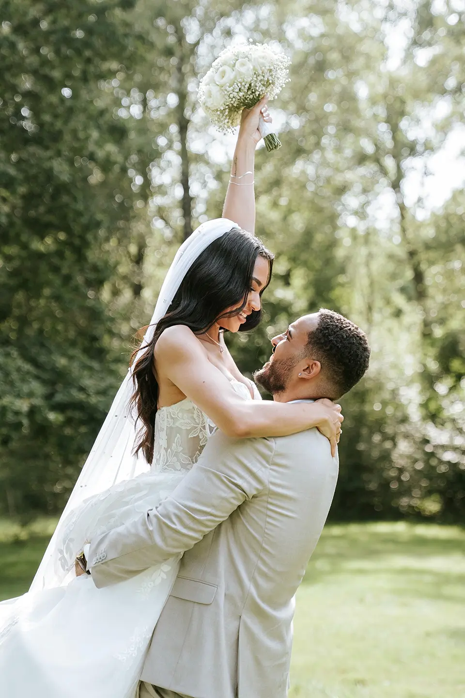 Bräutigam hebt die Braut im Park, sie streckt den Brautstrauß hoch – Berlin; natürliche Hochzeitsfotografie, emotionale Hochzeitsbilder
