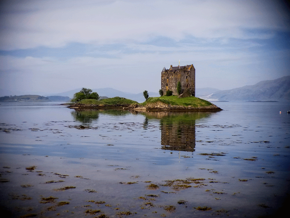Castle Stalker reflecting in calm waters, surrounded by misty mountains on the west coast of the Scottish Highlands ©Stephanie Dosch | theViatrix Scotland Private Luxury Travel
