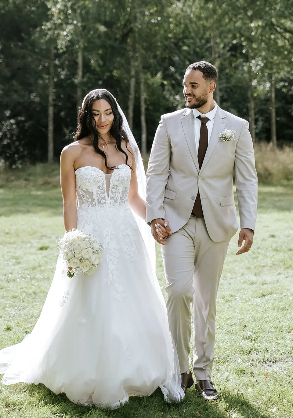 Die Braut führt den weißen Strauß, beide schreiten Hand in Hand über die Wiese. Natürliche Hochzeitsfotografie und hochzeitsfotograf für zwei mit ruhiger, eleganter Note