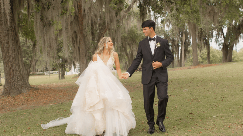 bride and groom walking holding hands under oak trees