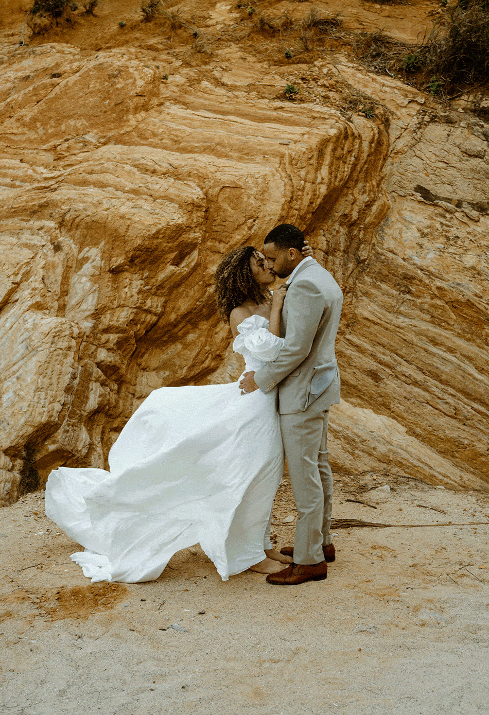 a gif of a bride and groom going in for a kiss while the brides dress flaps in the wind