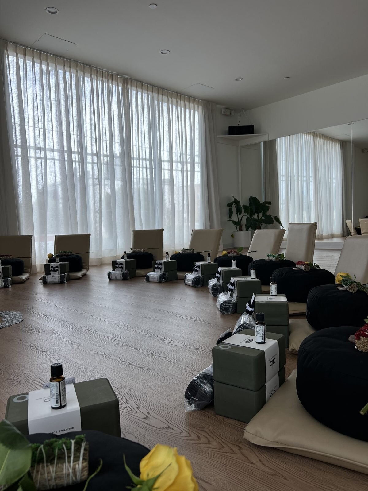 Ceremny studio set up for a facilitator training session with bolsters, yoga blocks, essential oil bottles, and yellow roses arranged on the wood floor before students arrive.