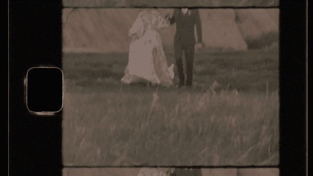 A video of a couple standing by a fence with large boulders in the background. The video then cuts to the couple walking forward with the shot only include the legs and torsos.