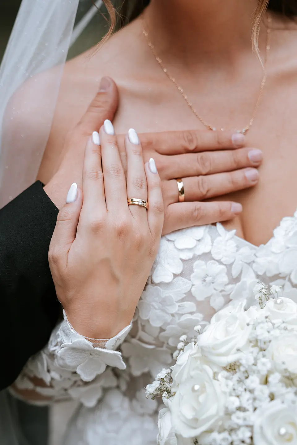 Die Hand der Braut mit Ring liegt auf der Brust des Bräutigams, Spitzenblüten und Strauß leuchten; fine art hochzeitsfotografie verbindet sich mit emotionale hochzeitsbilder