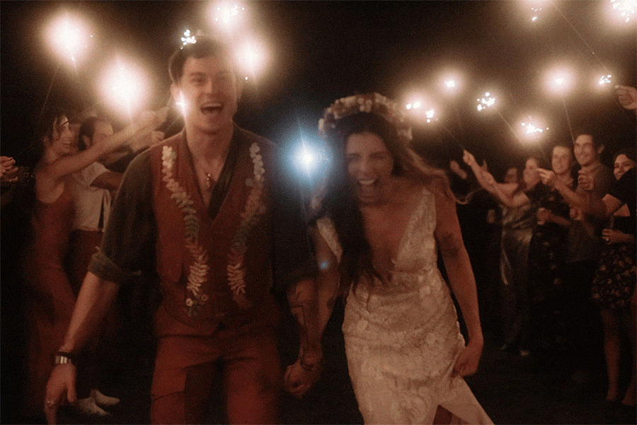 Bride and groom run through a sparkler tunnel at their Maine campground wedding, surrounded by cheering guests on a warm fall night