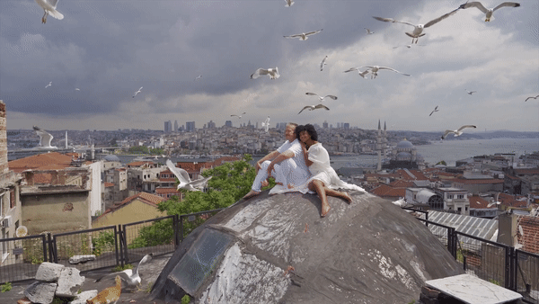 Couple sit atop a domed roof in Istanbul with birds flying around them